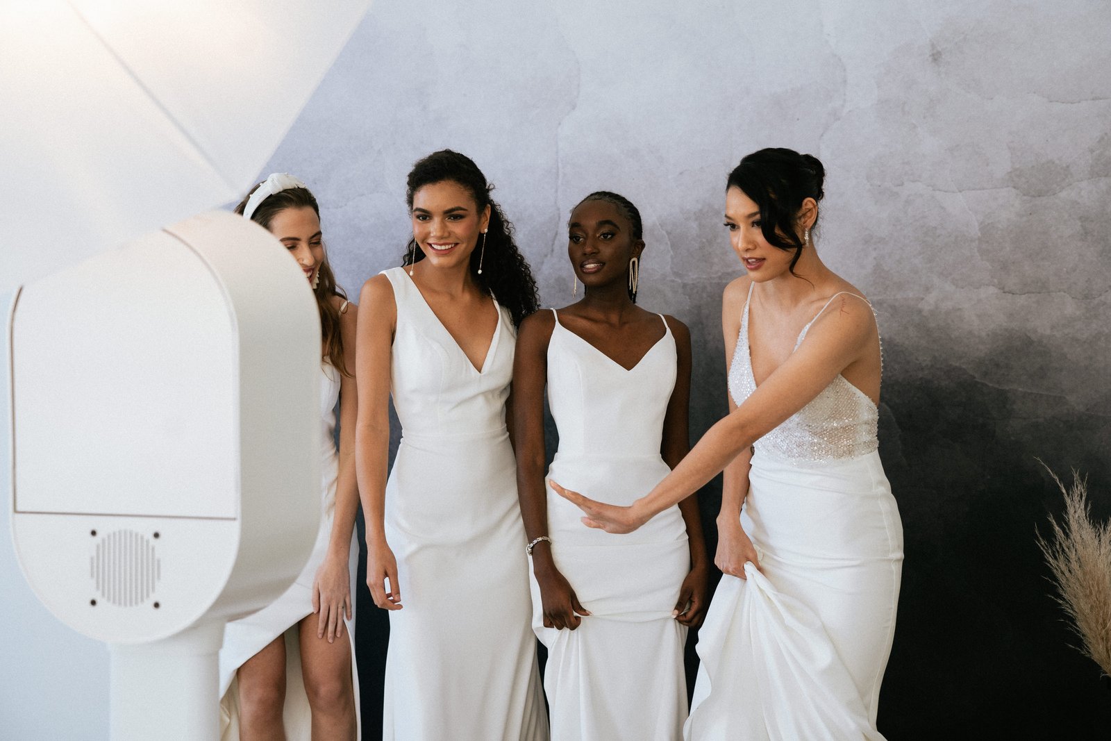 A bridal party in white dresses huddled together reviewing their photo strip